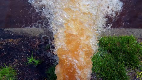 A-low,-top-down-shot-of-a-white-fire-hydrant-spraying-rusty-water-onto-the-street-on-a-sunny-day