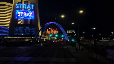 Driving-on-Las-Vegas-Strip-at-Night,-Landmark-Arch-Sign,-Strat-Casino-Hotel,-Street-Traffic-Lights