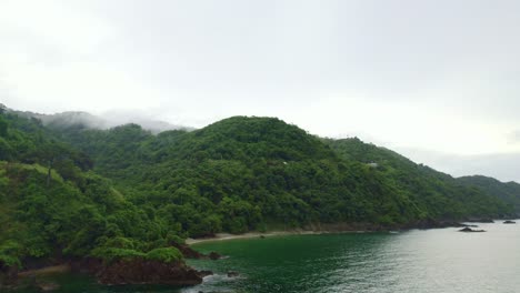 Drone-flying-over-ocean-with-boats-and-montain-filled-with-clouds