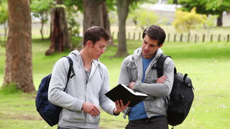 Man-using-a-book-to-explain-something-to-his-friend-who-has-his-arms-crossed