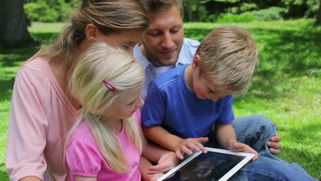 A-boy-sits-with-his-family-who-watches-as-he-presses-the-screen-of-a-tablet-pc
