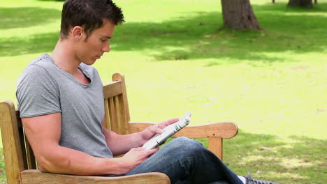 Man-reading-a-newspaper-while-sitting-on-a-wooden-bench