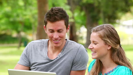 Woman-laughing-as-she-watches-a-laptop-with-her-friend-before-playfully-pushing-him