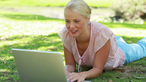 A-woman-lying-in-the-park-with-her-laptop-as-she-then-looks-at-the-camera