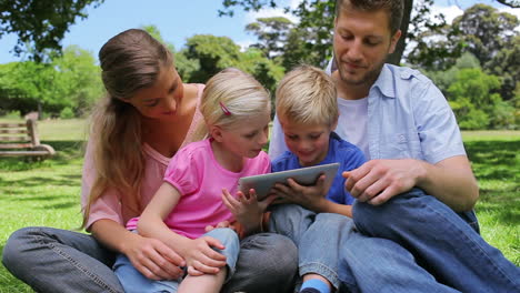 Familia-Sentada-Una-Al-Lado-De-La-Otra-Mientras-Usa-Una-Tableta-Que-Sostienen-Los-Niños