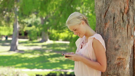 Eine-Frau-Steht-Neben-Einem-Baum-Und-Schaut-Auf-Ihr-Mobiltelefon