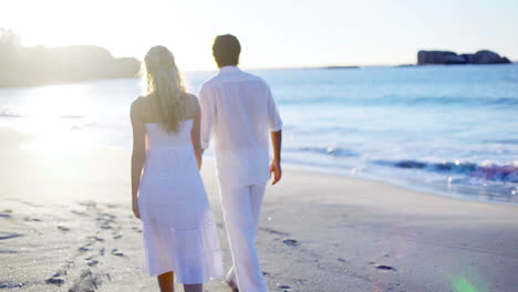 Una-Pareja-En-La-Playa-Caminando-Hacia-El-Atardecer-Mientras-Se-Toman-De-La-Mano.