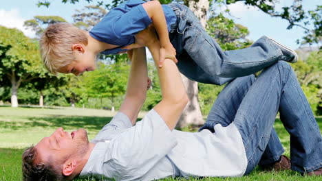 El-Padre-Se-Acuesta-En-El-Césped-Y-Levanta-A-Su-Hijo-En-El-Aire-Mientras-Finge-Ser-Un-Avión.