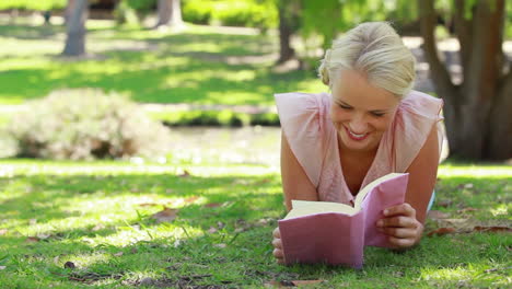 A-woman-reading-a-book-lying-in-the-park-as-she-then-looks-at-the-camera