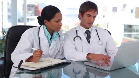 Doctor-using-a-laptop-while-his-colleague-is-taking-notes