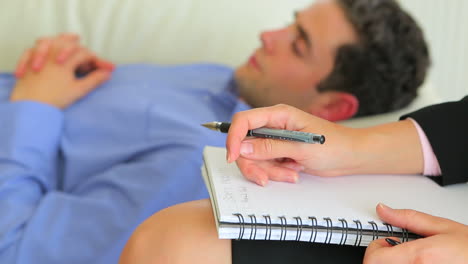 Man-lying-on-a-sofa-while-with-therapist-making-notes