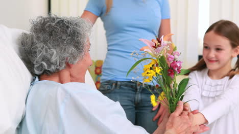 Mujer-Y-Niña-Ofreciendo-Flores-A-Una-Anciana-En-Una-Cama-De-Hospital.