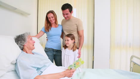 Family-standing-together-around-a-hospital-bed-while-a-patient-is-reading-a-card