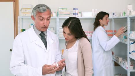 Pharmacist-pointing-at-a-flask-of-pills-in-front-of-a-customer