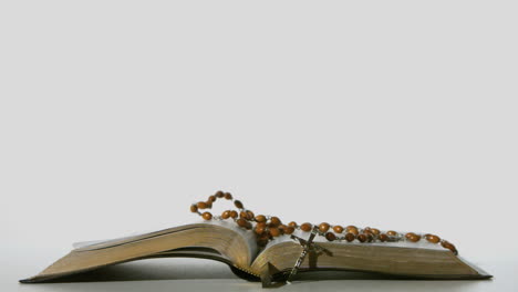 Rosary-beads-falling-onto-open-bible-on-white-background
