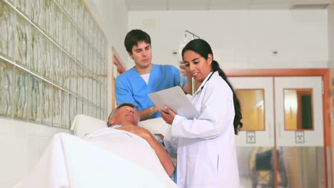 Un-Médico-Sonriente-Y-Un-Enfermero-Revisando-A-Un-Paciente-Acostado-En-Una-Cama