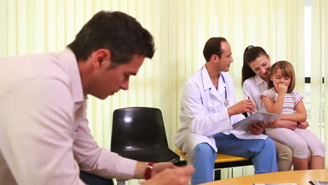 Smiling-doctor-talking-to-a-girl-while-she-sits-on-the-knees-of-her-mother