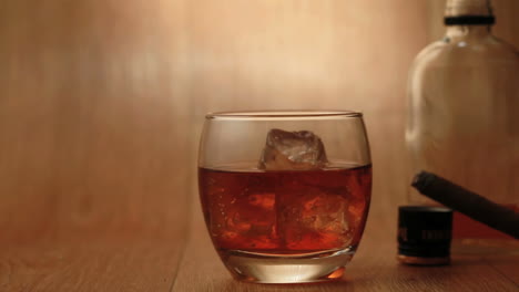 Cigar-being-smoked-beside-tumbler-of-whiskey-on-the-rocks