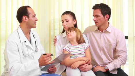 Doctor-talking-to-a-smiling-girl-while-she-sits-on-the-knees-of-a-woman