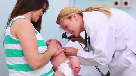 Mother-holding-a-baby-in-an-examination-room-with-a-doctor-using-an-otoscope