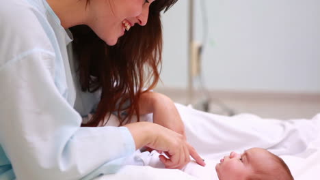 Mother-sitting-on-a-bed-while-smiling-to-a-new-born-baby