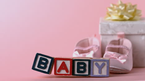 Umgestürzte-Babybausteine-Mit-Babyschuhen-Und-Geschenkkarton-Im-Hintergrund