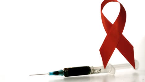 Syringe-dropping-down-beside-a-red-ribbon-