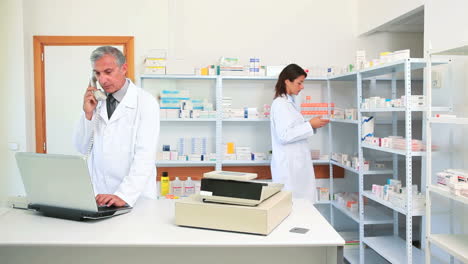 Farmacéutico-Hablando-Por-Teléfono-En-Una-Farmacia-Con-Otro-Farmacéutico