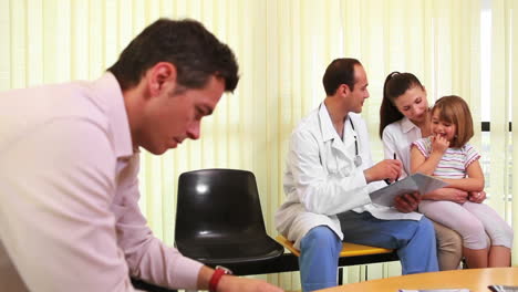 Doctor-talking-to-a-smiling-girl-while-she-sits-on-the-knees-of-her-mother