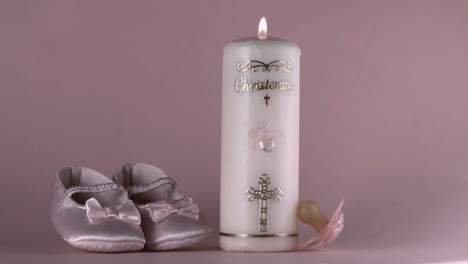 Pacifier-falling-beside-lit-baptism-candle-and-baby-shoes