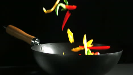 Mixed-peppers-falling-into-wok-on-black-background