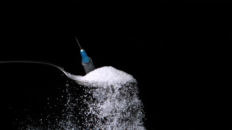 Syringe-falling-onto-spoon-of-sugar-on-black-background