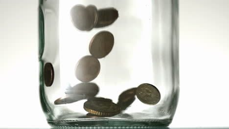 Many-coins-pouring-into-glass-jar-close-up-on-white-background