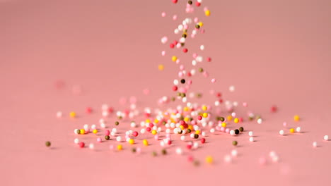Loads-of-sprinkles-falling-on-pink-surface