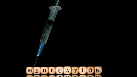 Syringe-falling-in-front-of-dice-spelling-medication-on-black-background