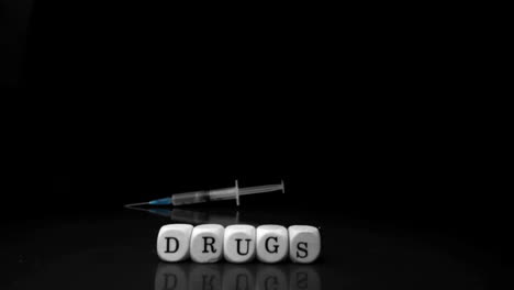 Syringe-falling-and-rolling-towards-white-dice-spelling-drugs