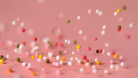 Loads-of-sprinkles-falling-on-pink-surface-and-rolling-across