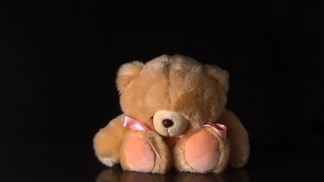 Teddy-bear-with-pink-ribbon-falling-on-black-background