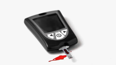 Drop-of-blood-falling-onto-test-strip-of-blood-glucose-monitor-on-white-background