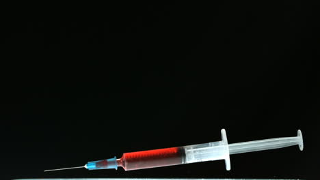 Syringe-of-blood-falling-and-bouncing-on-black-surface