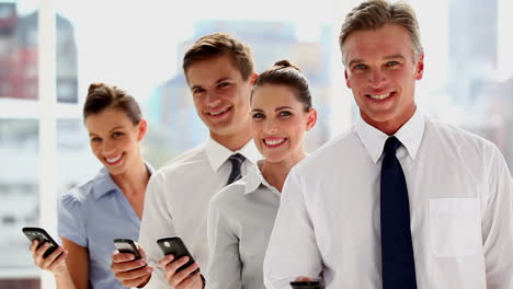 Business-people-standing-in-line-with-their-smartphones