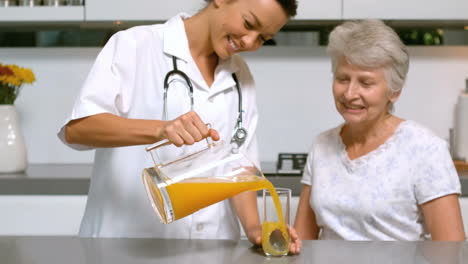 Home-help-pouring-orange-juice-for-patient-in-kitchen