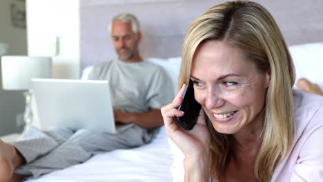 Woman-laughing-while-she-is-on-the-phone-next-to-his-husband-on-his-laptop