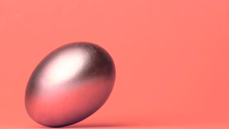 Shiny-egg-rolling-across-pink-surface