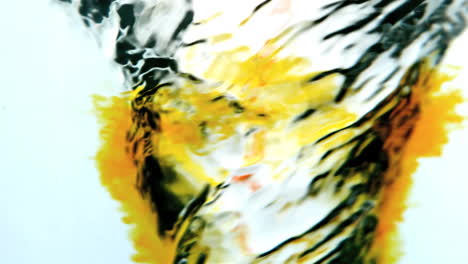 Yellow-ink-swirling-into-water-whirlpool-on-white-background