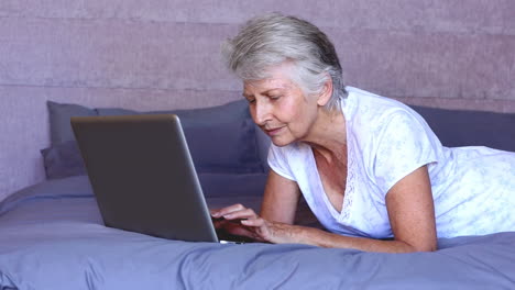 Woman-lying-on-bed-using-laptop