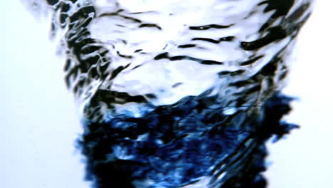 Blue-ink-swirling-into-water-whirlpool-on-white-background