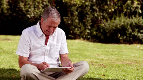Mature-man-sat-on-the-grass-using-his-tablet-computer