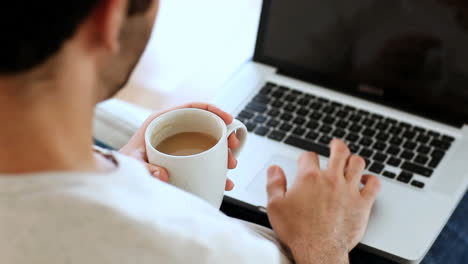 Man-drinking-a-coffee-while-using-his-laptop