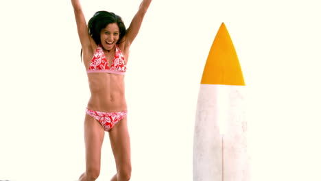 Smiling-woman-jumping-next-to-her-surfboard